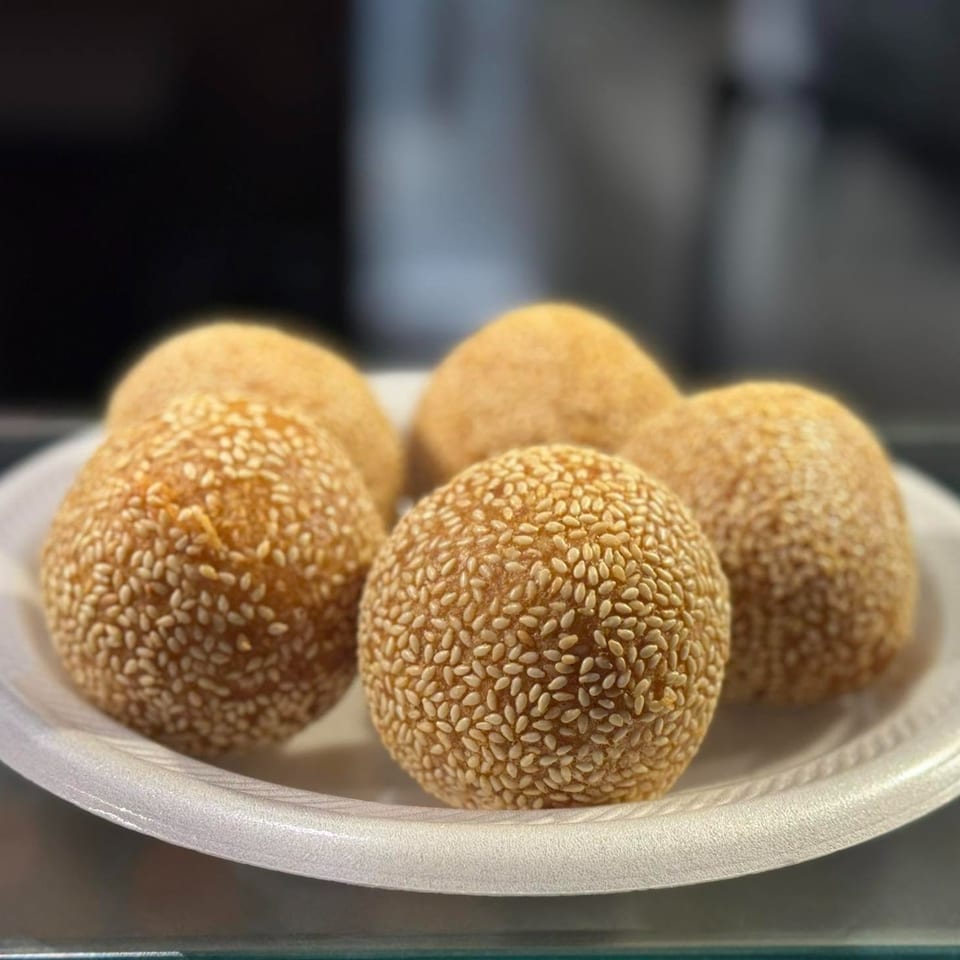 Five golden-brown sesame balls, coated in white sesame seeds, arranged on a white paper plate.