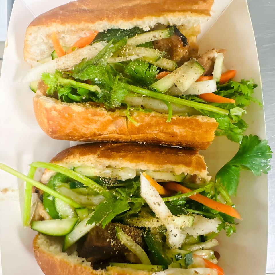 Two Whata Pho banh mi sandwiches, filled with meat, cilantro, cucumbers, carrots, and onions.